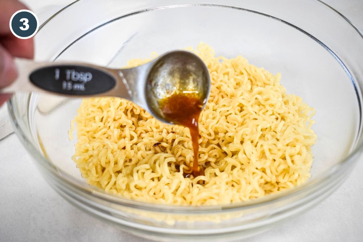 Pouring sesame dressing onto freshly cooked ramen noodles in a glass bowl.
