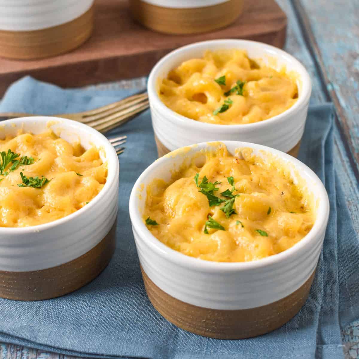 Three ramekins of baked mac and cheese on a blue napkin, ready to serve.