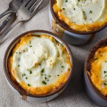 Close-up of baked mini shepherd’s pies in ramekins with golden edges and mashed potato swirls, sprinkled with parsley.