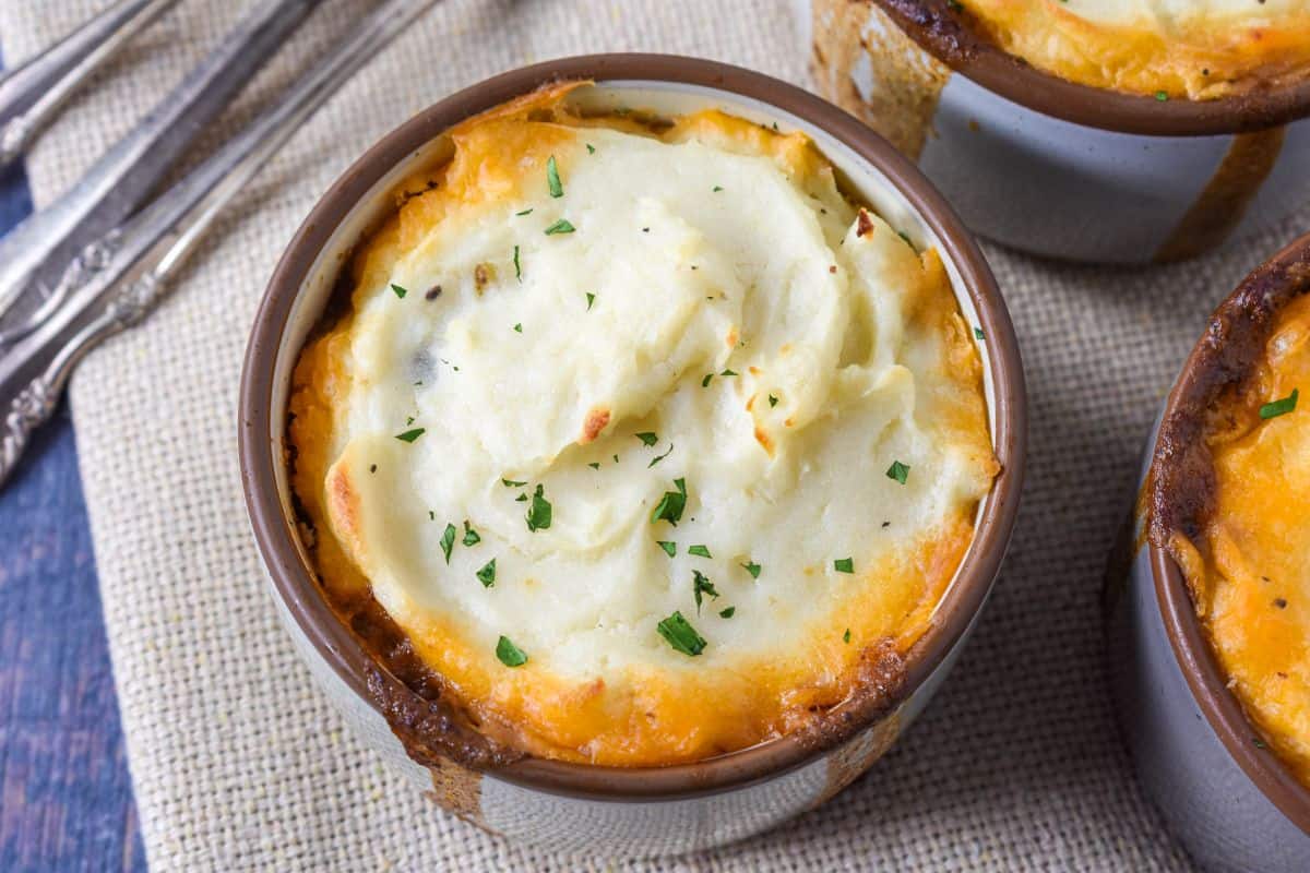 Close-up of baked mini shepherd’s pies in ramekins with golden edges and mashed potato swirls, sprinkled with parsley.