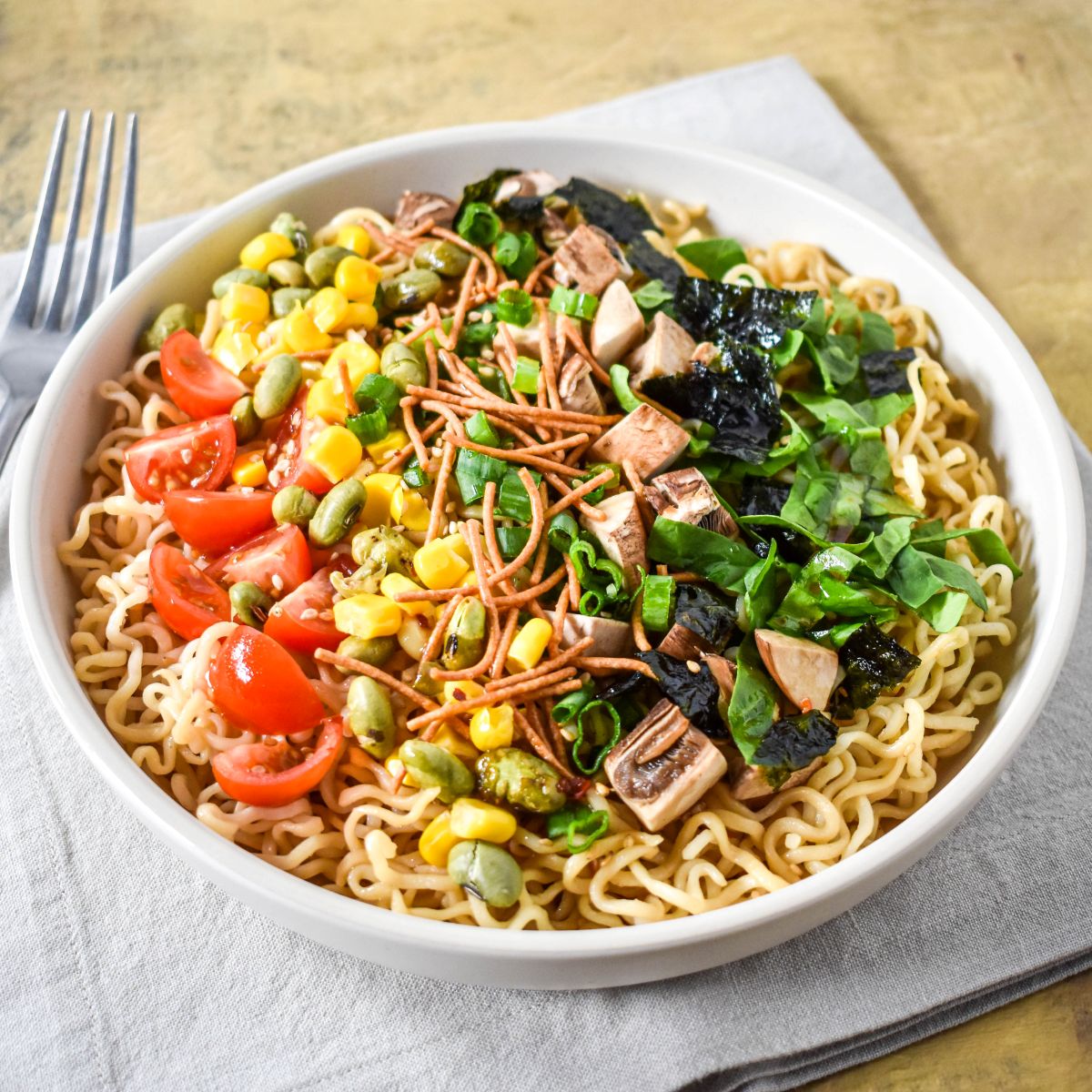 Bright side-angle of sesame ramen noodle salad in a white bowl on a neutral napkin.