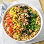 Overhead view of sesame ramen noodle salad with colorful toppings arranged in sections.