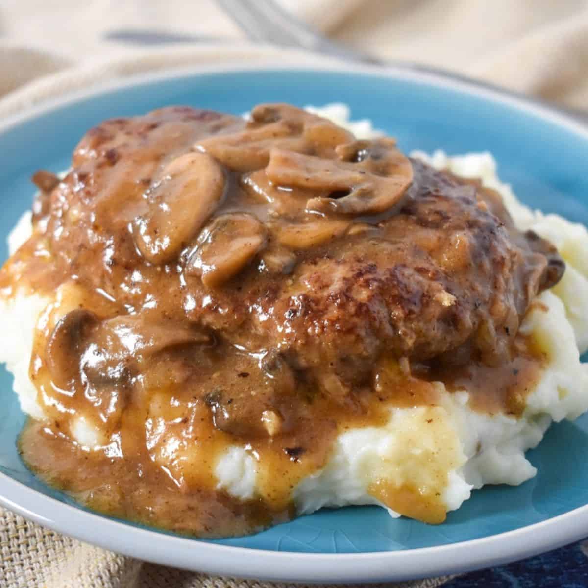 The finished turkey Salisbury steak served on a bed of mashed potatoes on a blue plate with a beige linen.