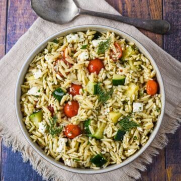 Overhead view of herb orzo salad in a bowl, garnished with fresh dill and served with a spoon.