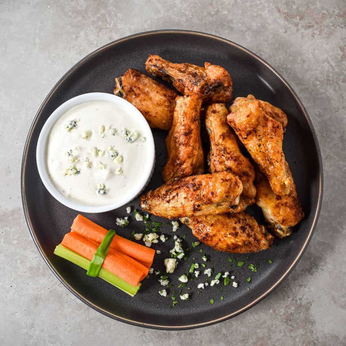 Plate of wings with vegetables and a small bowl of dressing for dipping.