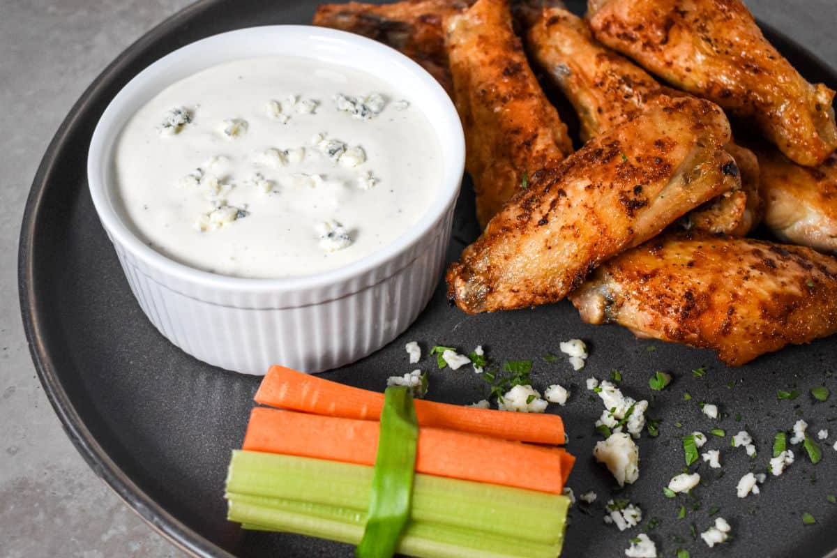 Another view of wings, veggie sticks, and dressing, garnished with crumbled cheese and herbs.