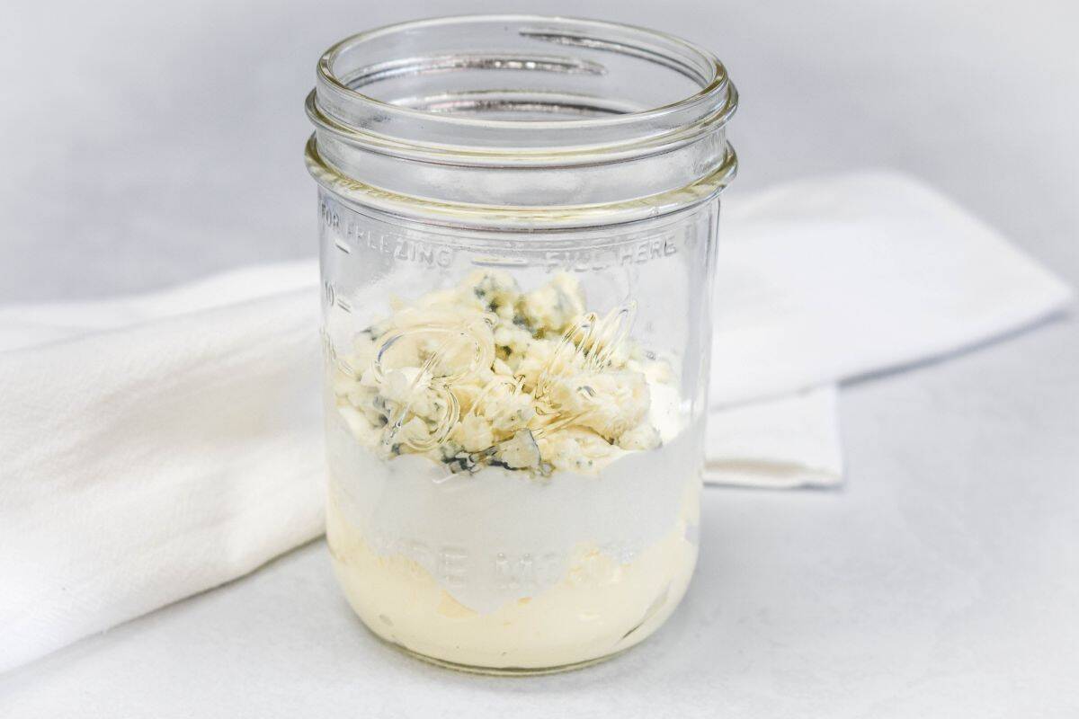 Mayo, sour cream, and blue cheese added to a glass jar before mixing.