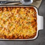 A close-up overhead shot of the entire vodka sauce pasta bake in a casserole dish, showing the bubbly, golden cheese topping.