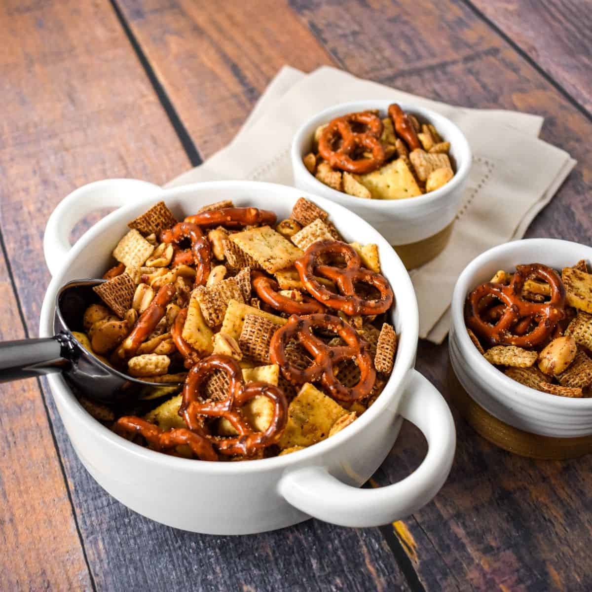 Finished snack mix in a white serving bowl with pretzels, crackers, cereal, and peanuts, ready to serve.