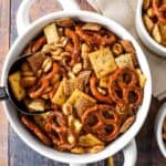 Large white bowl filled with homemade Cajun party mix made with pretzels, peanuts, cereal, and crackers. Topped with bold seasoning, this crunchy snack is perfect for game day or parties.