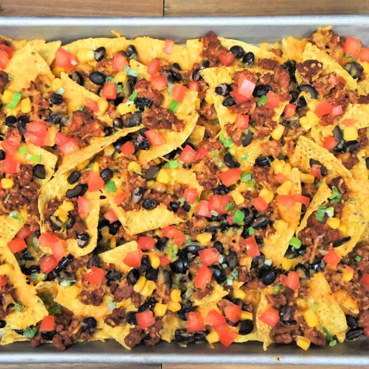 Loaded sheet pan nachos topped with ground turkey, melted cheese, black beans, corn and diced tomatoes