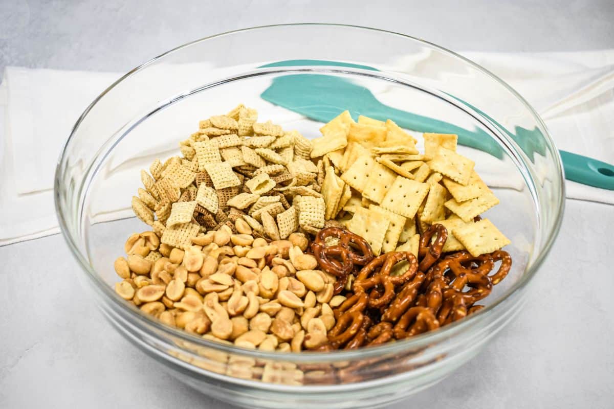 Large glass bowl with rice cereal, wheat cereal, pretzels, peanuts, and mini saltine crackers.