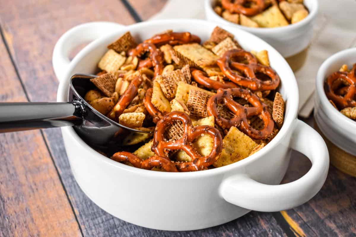 Finished snack mix in a white serving bowl with pretzels, crackers, cereal, and peanuts, ready to serve.