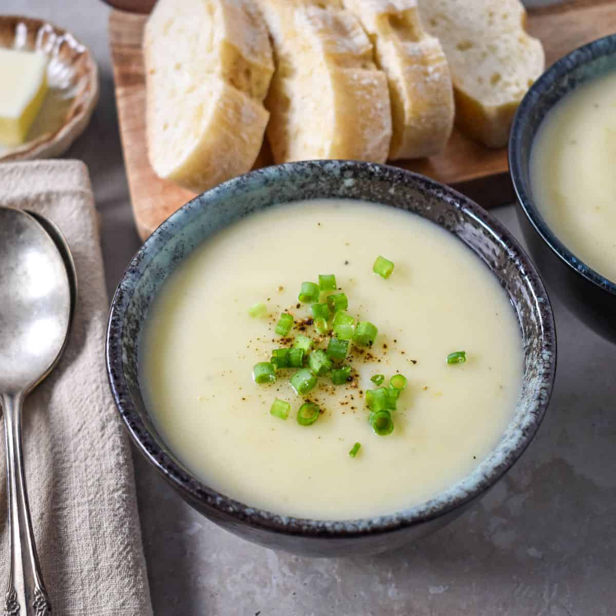 Side angle view of creamy soup in a bowl, with bread slices in the background.