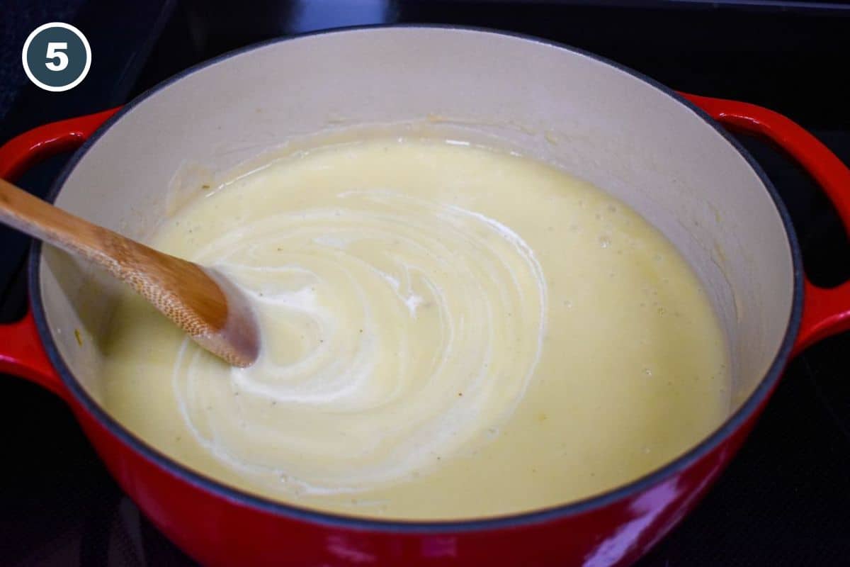 Stirring cream into the blended potato leek soup in a Dutch oven.