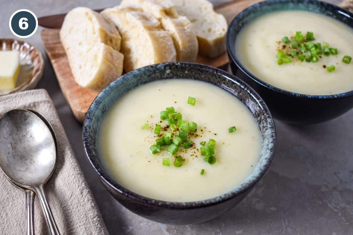 Two bowls of creamy potato leek soup garnished with green onions, served with sliced bread.