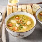 Bowl of chicken and stars soup with carrots, chicken pieces, and stelline pasta, served with slices of bread on a wooden board.