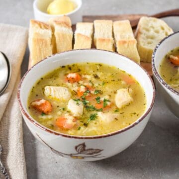 Bowl of chicken and stars soup with carrots, chicken pieces, and stelline pasta, served with slices of bread on a wooden board.