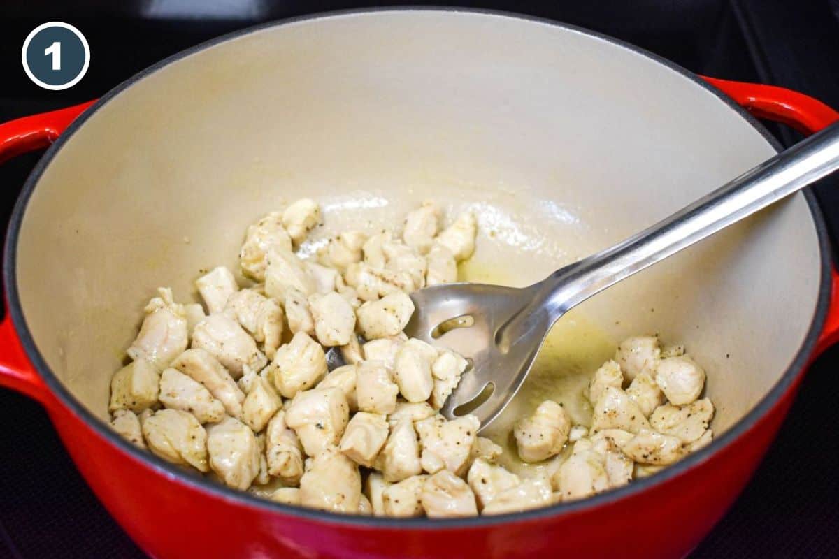 Chicken pieces cooking in a red Dutch oven with a slotted spoon.