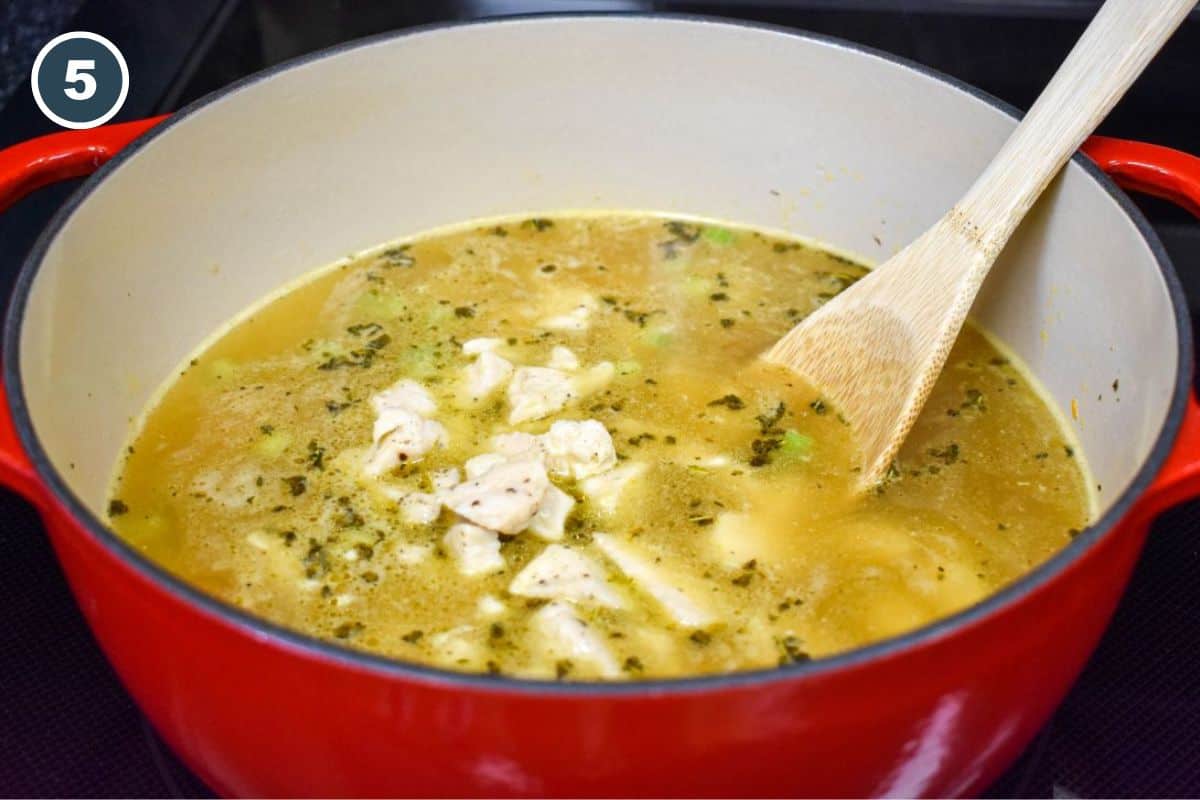 Chicken simmering in the broth mixture with a wooden spoon.