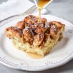 French toast casserole topped with powdered sugar and syrup being poured on top.