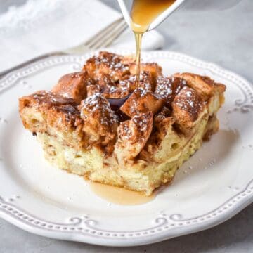 French toast casserole topped with powdered sugar and syrup being poured on top.