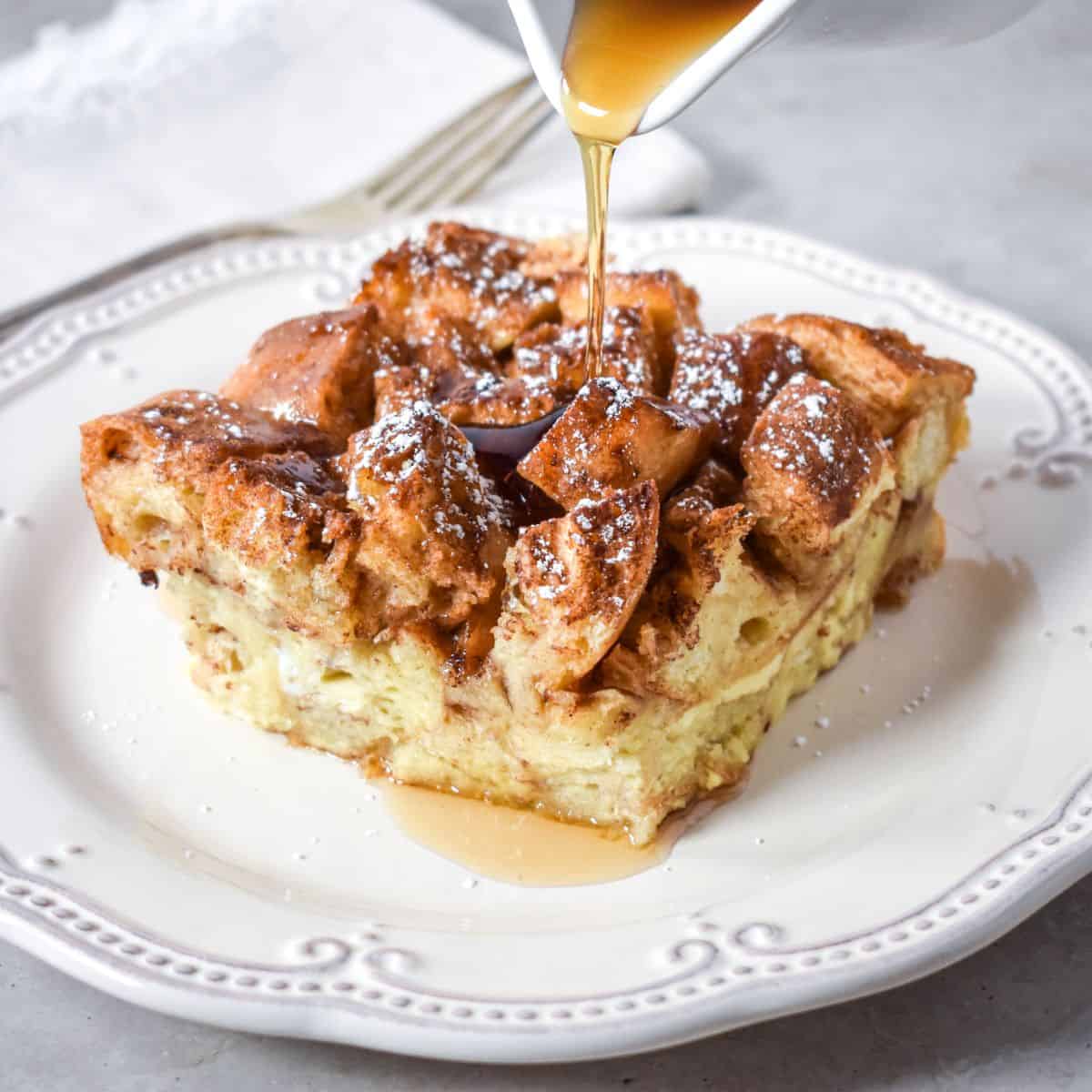French toast casserole topped with powdered sugar and syrup being poured on top.