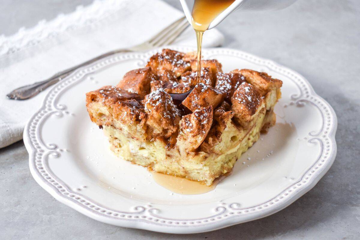 French toast casserole topped with powdered sugar and syrup being poured on top.