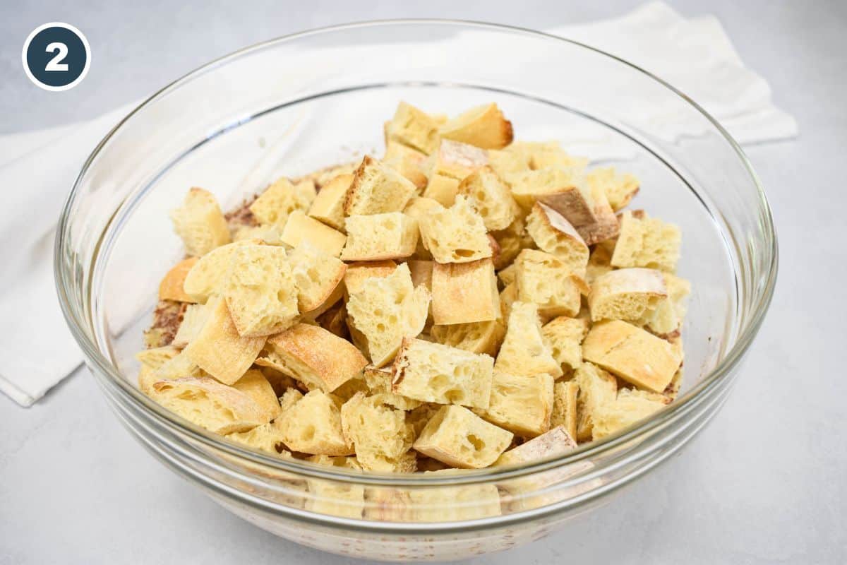 Cubed bread pieces added to the custard mixture in a glass bowl.