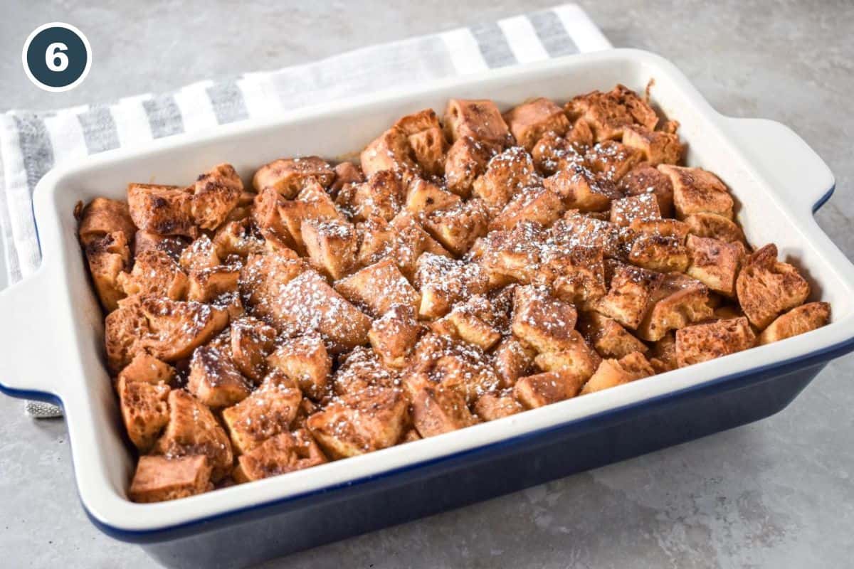 Baked French toast casserole topped with powdered sugar in a white dish.