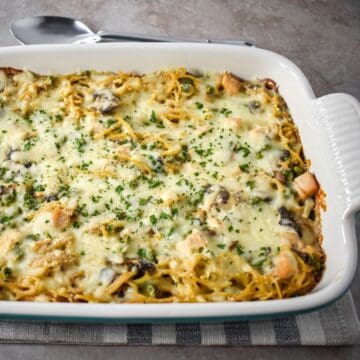 Turkey tetrazzini casserole fresh from the oven, topped with melted cheese and parsley in a white baking dish.