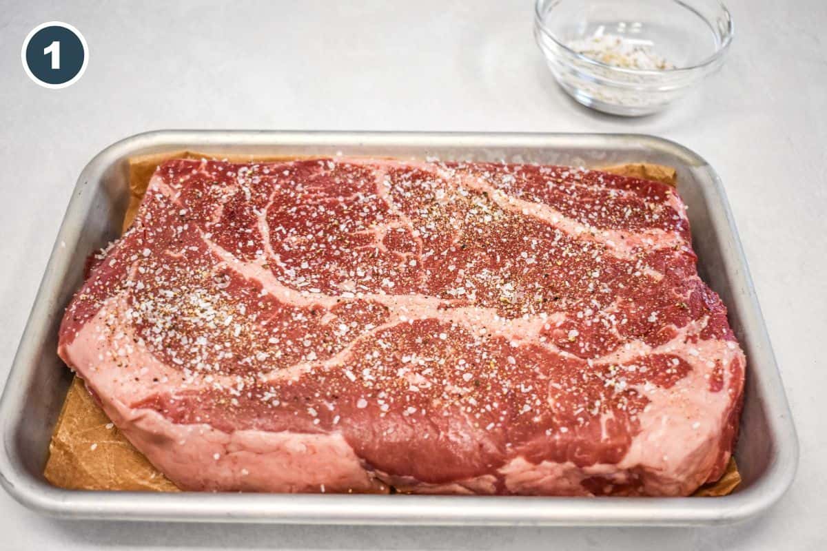 Chuck roast on a small tray, seasoned with salt, pepper, garlic powder, and onion powder.