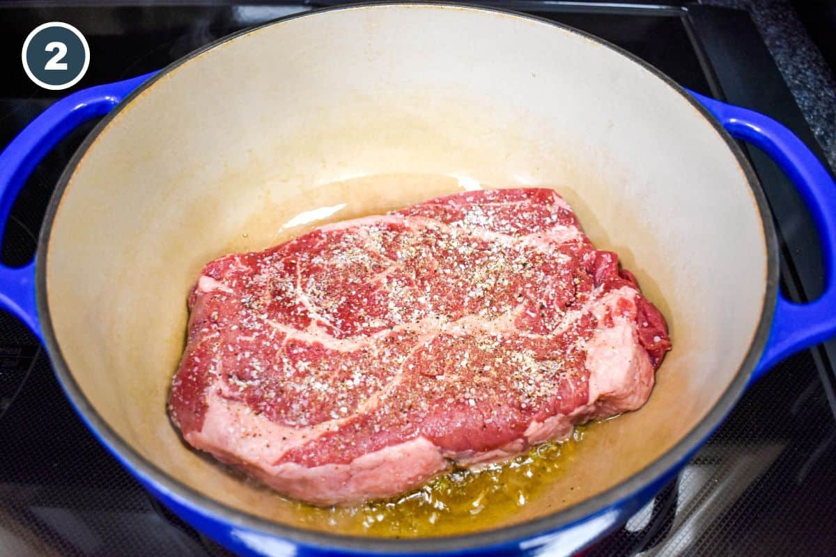 Seasoned chuck roast placed in a Dutch oven with hot oil to begin browning.