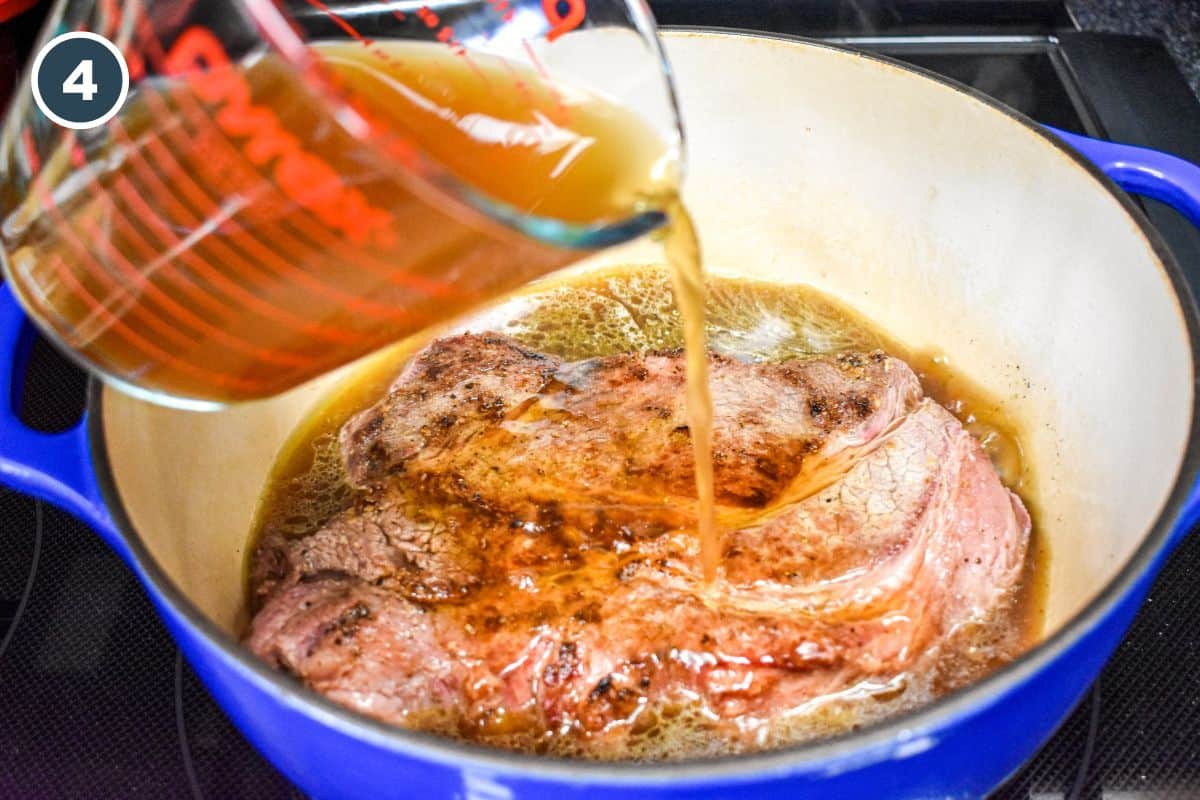 Beef broth being poured over the browned roast in the Dutch oven.