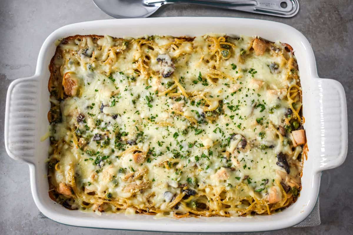 The baked casserole in a white dish topped with melted cheese and parsley after coming out of the oven.
