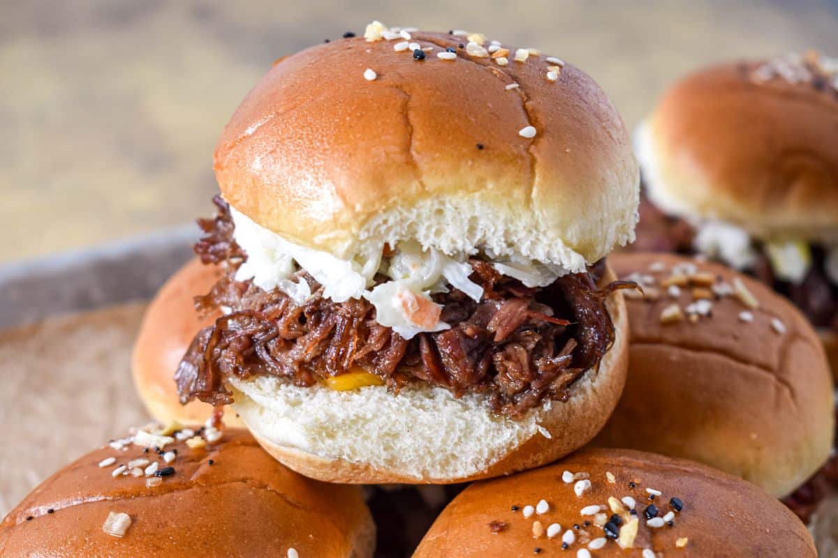 A close-up of one slider showing tender beef and coleslaw inside a soft bun.