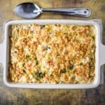 Baked turkey and rice casserole in a white dish, topped with crispy fried onions, with a serving spoon placed above the pan.