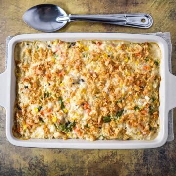 Baked turkey and rice casserole in a white dish, topped with crispy fried onions, with a serving spoon placed above the pan.