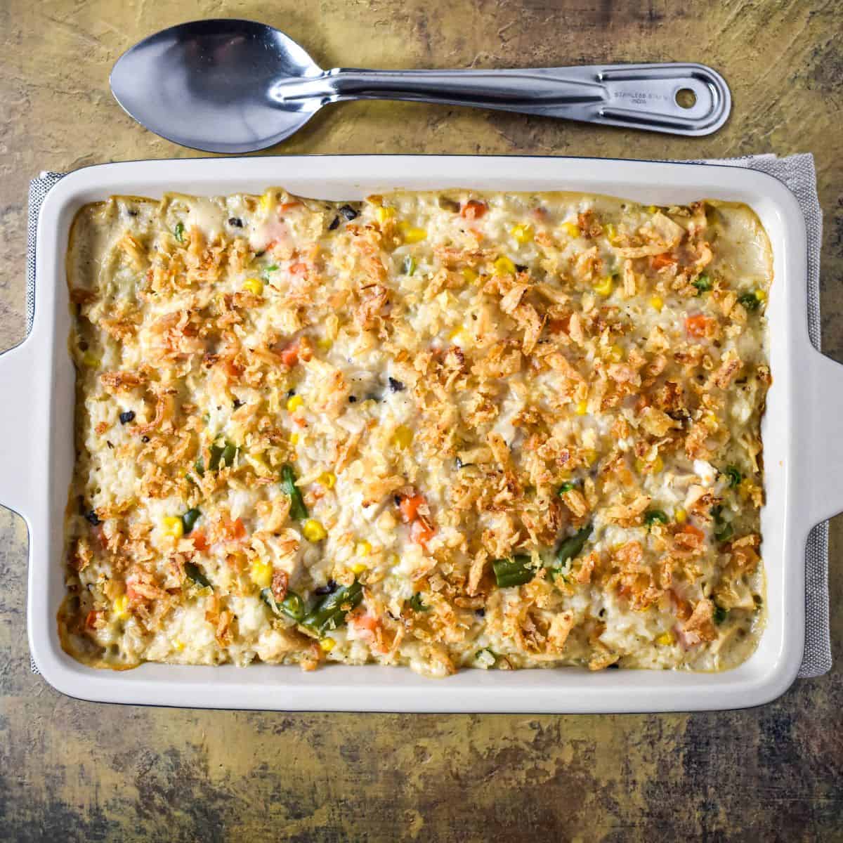 Baked turkey and rice casserole in a white dish, topped with crispy fried onions, with a serving spoon placed above the pan.