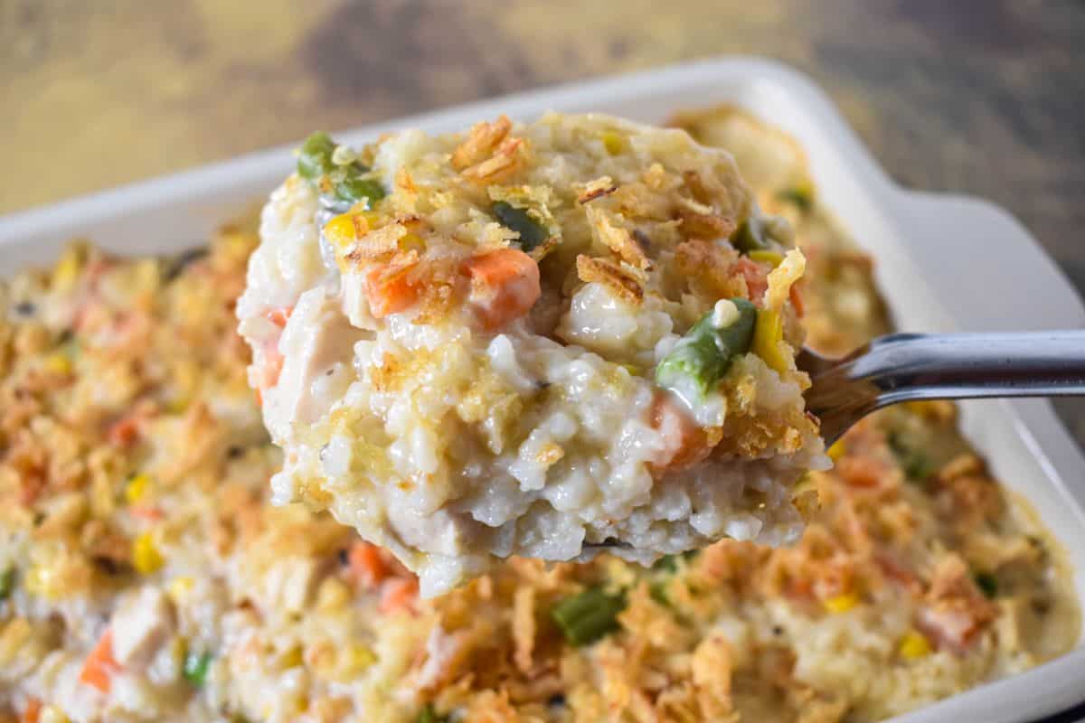 A spoonful of the creamy casserole lifted from the pan, showing rice, turkey, vegetables, and a crispy topping.