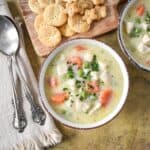 Overhead view of a bowl of turkey pot pie soup with carrots, peas, and parsley, served with crackers and spoons on the side.