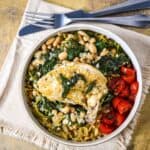 Airline chicken with cannellini beans served over orzo with wilted greens and cherry tomatoes in a shallow bowl.