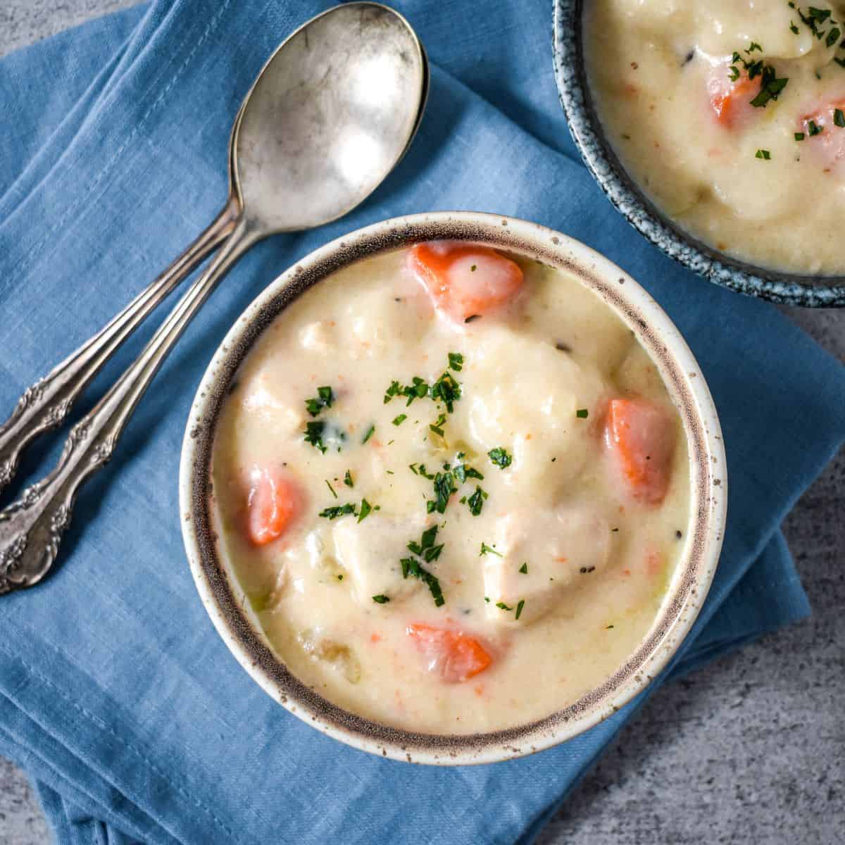 Creamy soup served in a rustic ceramic bowl on a blue linen napkin, with a second bowl and spoons nearby.