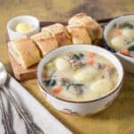 Two bowls of Italian sausage gnocchi soup with spinach and vegetables, served with crusty bread and butter on the side.