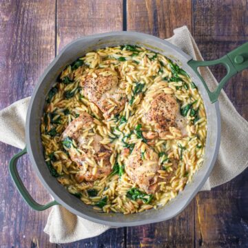 Creamy chicken orzo in a skillet with browned chicken thighs, spinach, and a creamy sauce.