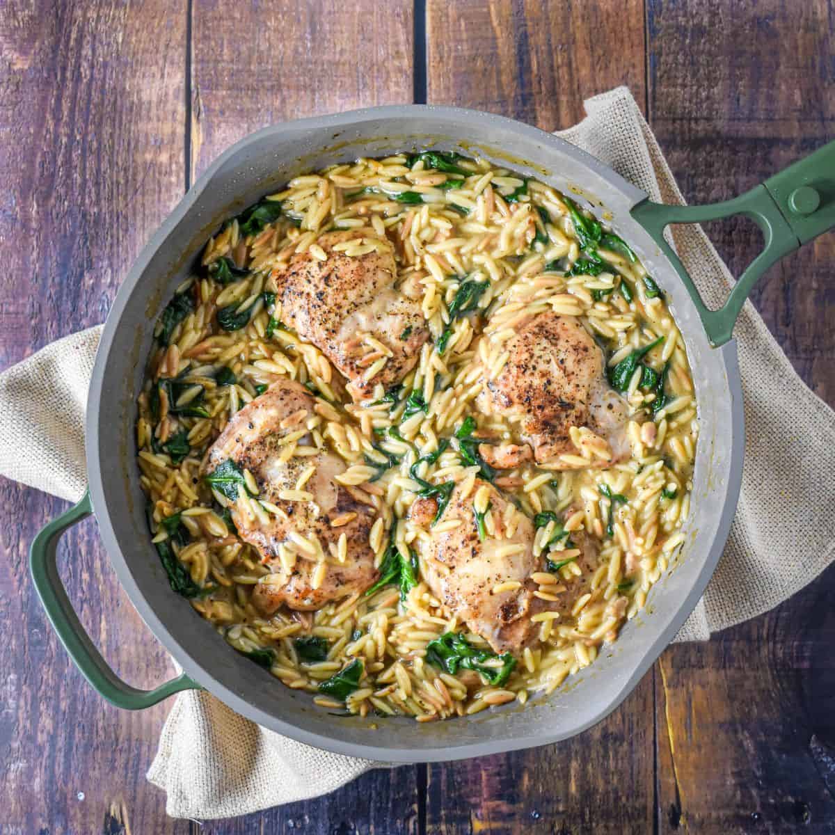 Creamy chicken orzo in a skillet with browned chicken thighs, spinach, and a creamy sauce.