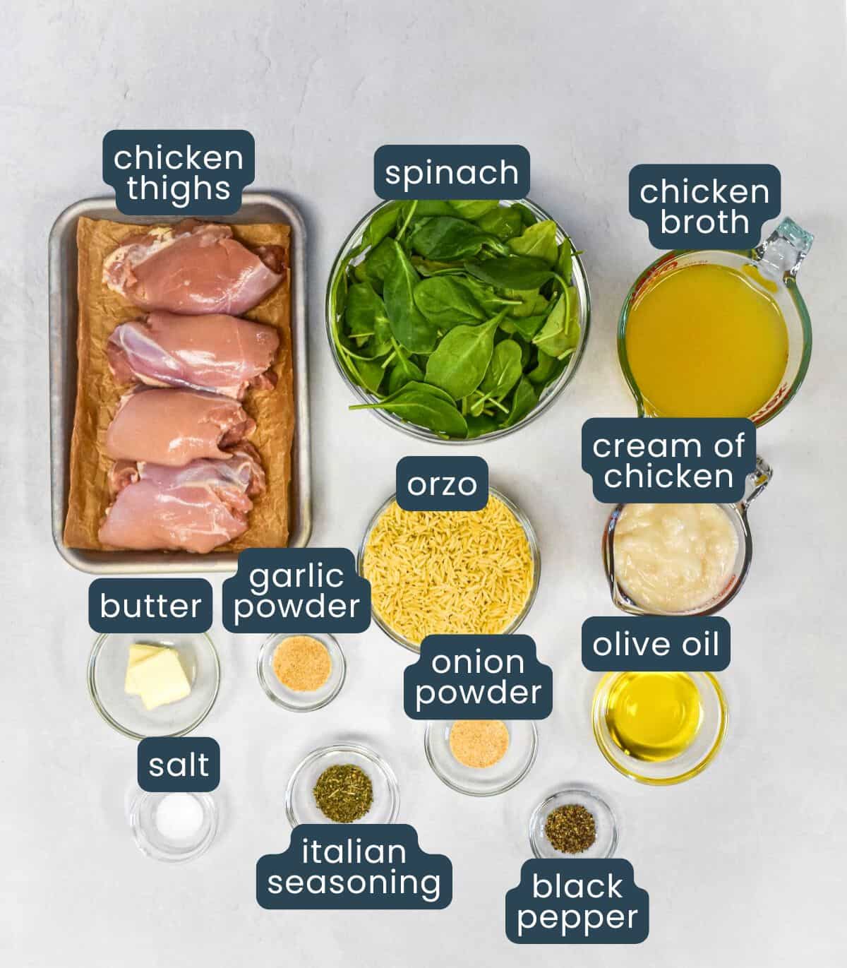 The ingredients for this dish include, chicken thighs, orzo, spinach, chicken broth, cream of chicken soup, olive oil, butter, and seasonings, set on a white table with each labeled.