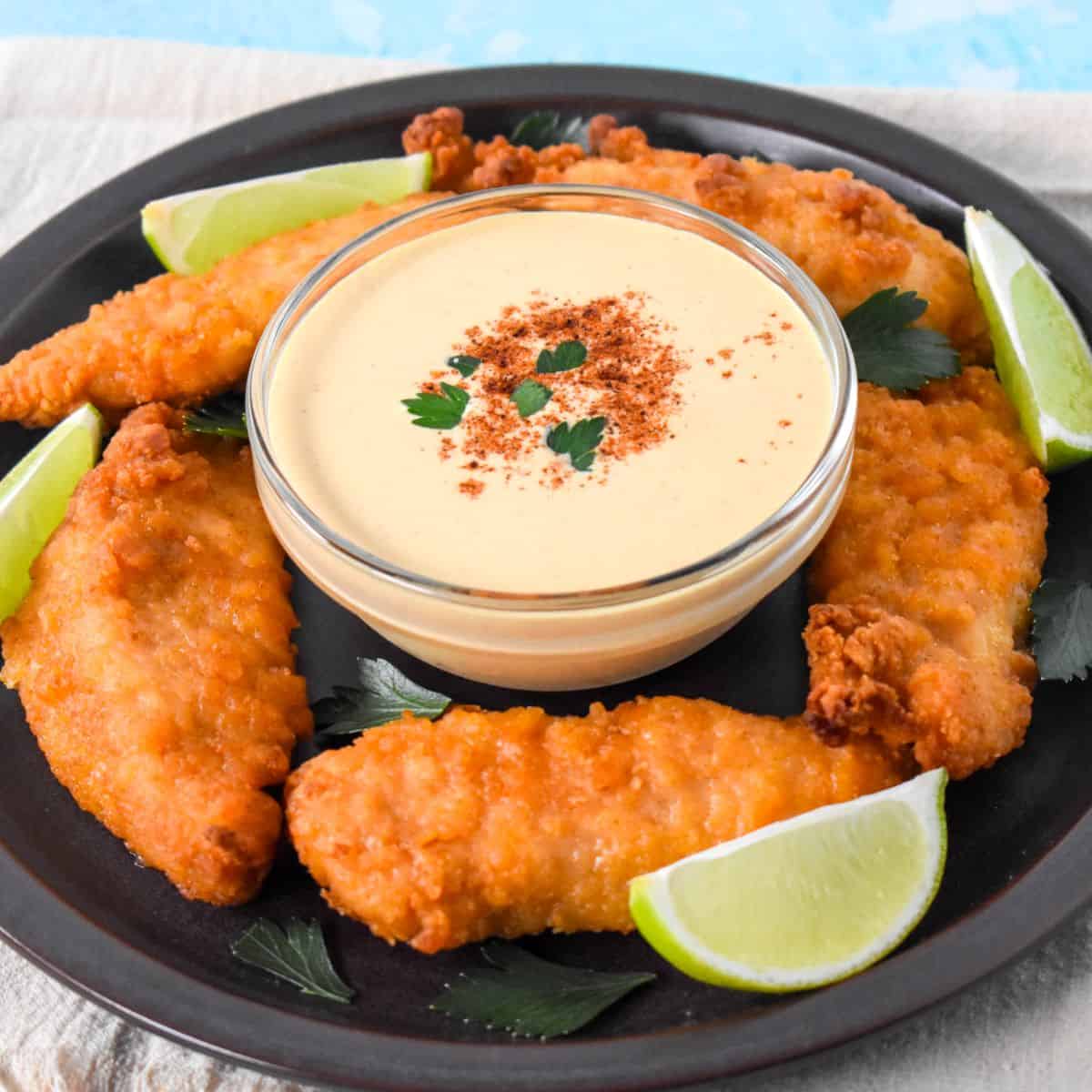 Creamy chipotle sauce served in a bowl with crispy chicken tenders and lime wedges on a plate.