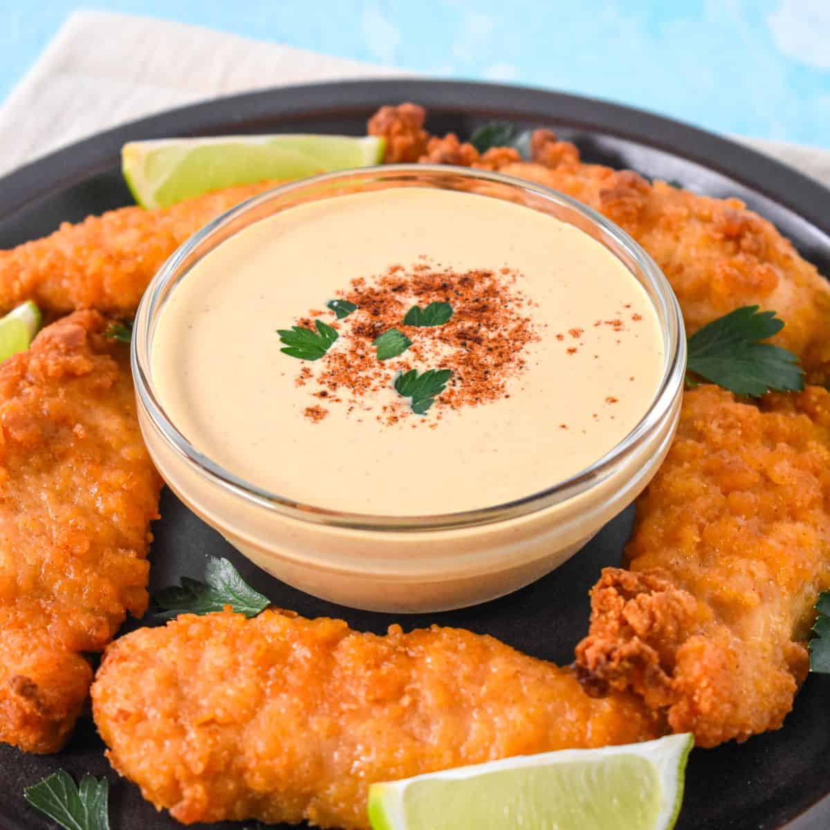 Creamy chipotle sauce in a bowl surrounded by crispy chicken tenders, garnished with parsley and served with lime wedges.