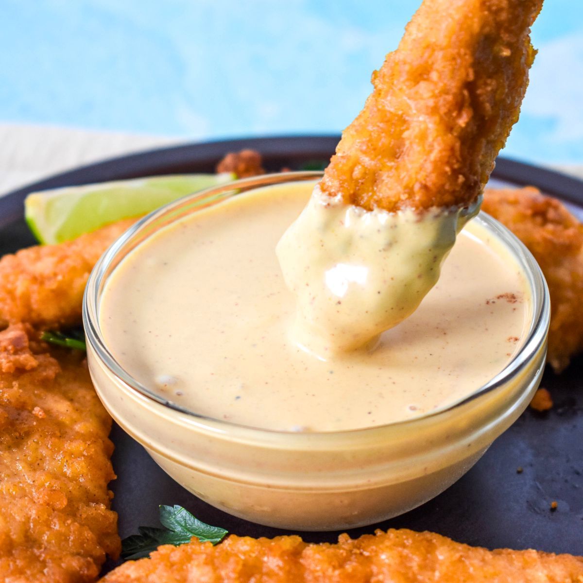 Close-up of a chicken tender dipped into a bowl of creamy chipotle sauce, showing the smooth, thick texture.